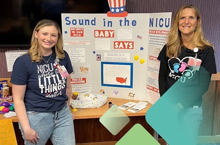 Two nurses with a trifold tabletop poster titled “Sound in the NICU.” 